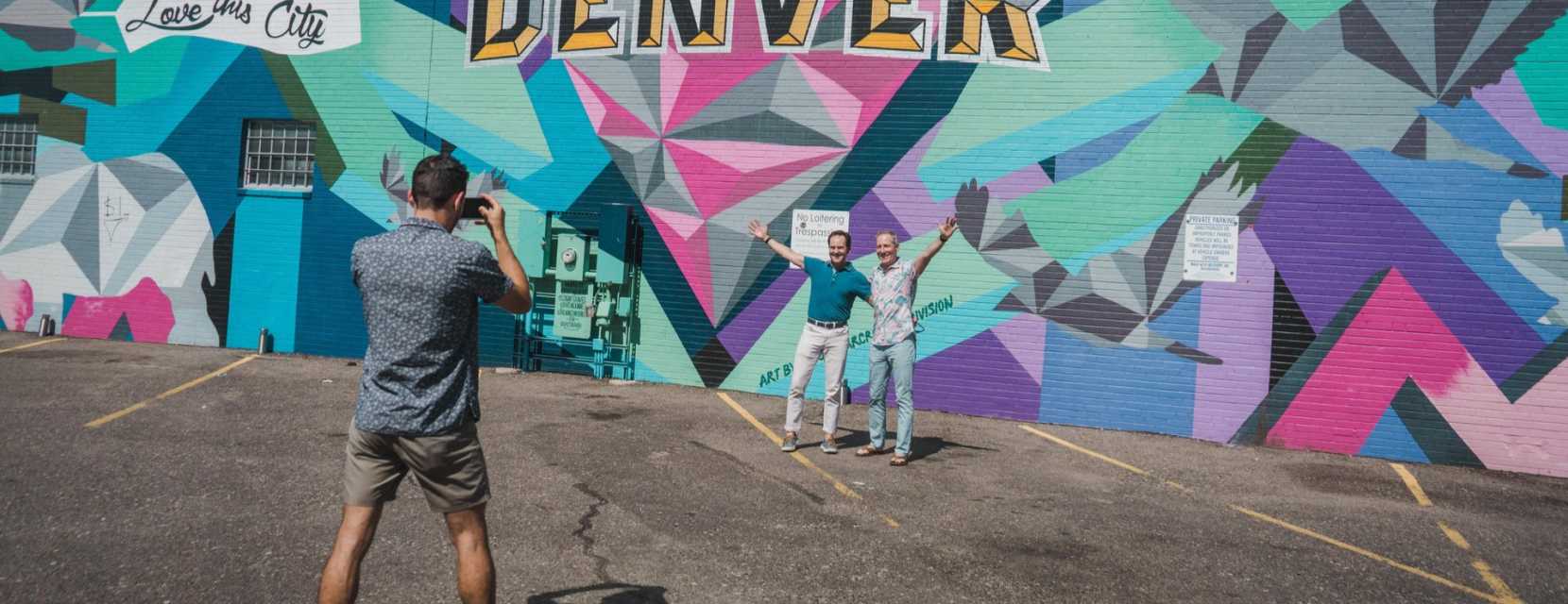 People pose and take a photo in front of the Love This City mural in Denver