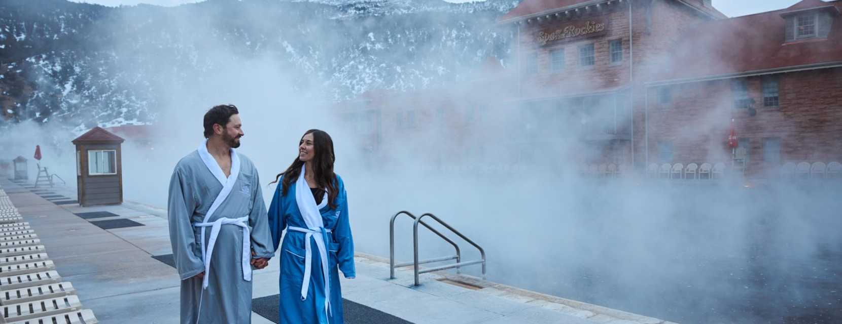 Two people wearing robes walk along the poolside at Glenwood Hot Springs Pool