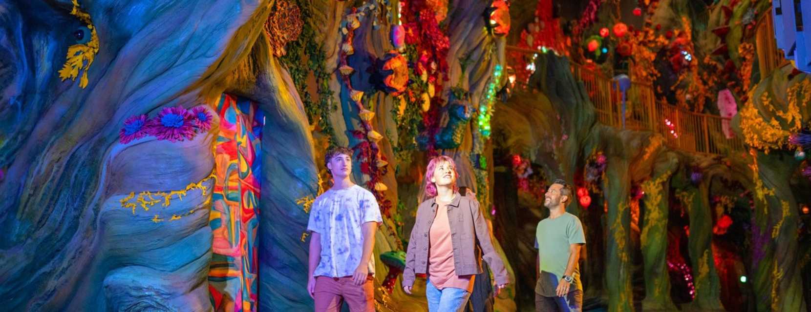 Three people look around in wonder at a glowing, nature-themed exhibit in Meow Wolf