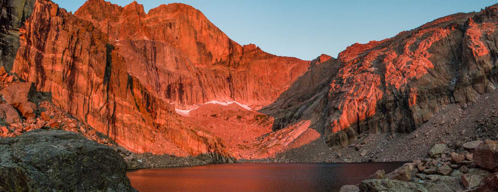 A rocky mountain peak is aglow and reflected in a lake in Rocky Mountain National Park.