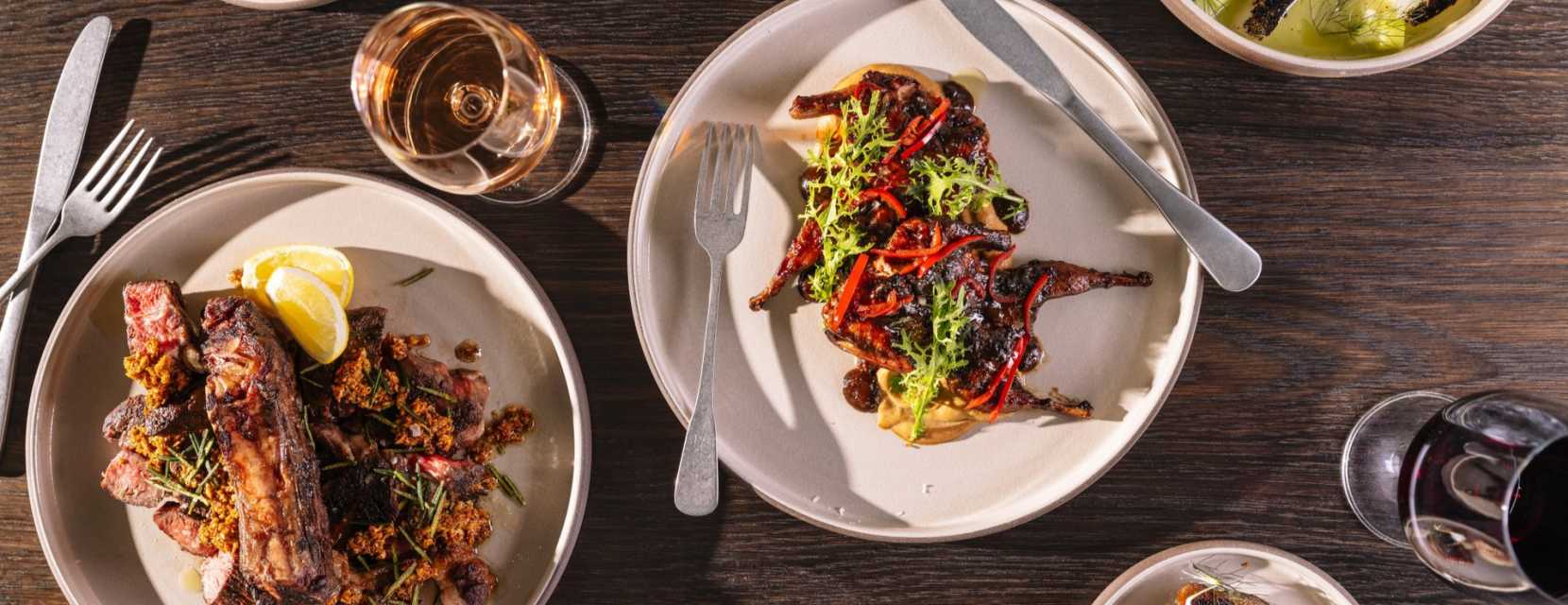 An assortments of plated meat dishes at Stellar Jay with a glass of wine