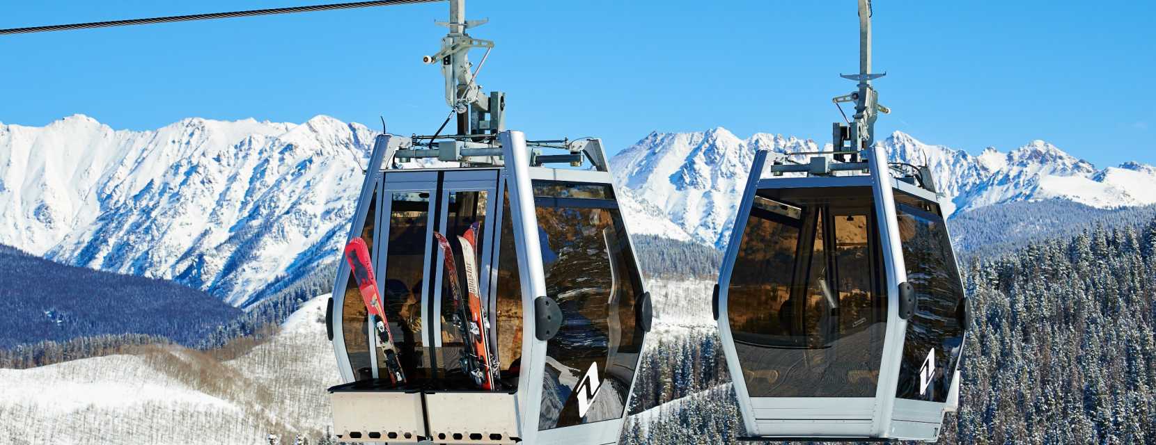 Two gondolas float about Vail Mountain with snow-covered Gore Range in the background