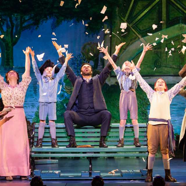 theatre stage with cast raising arms into air