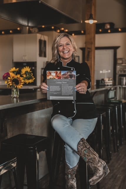 Dawn from Farm Fusion sitting in her kitchen holding a flyer that says cooking classes.
