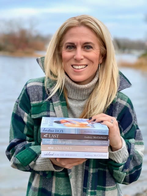 Author Audrey McClelland holding stack of novels