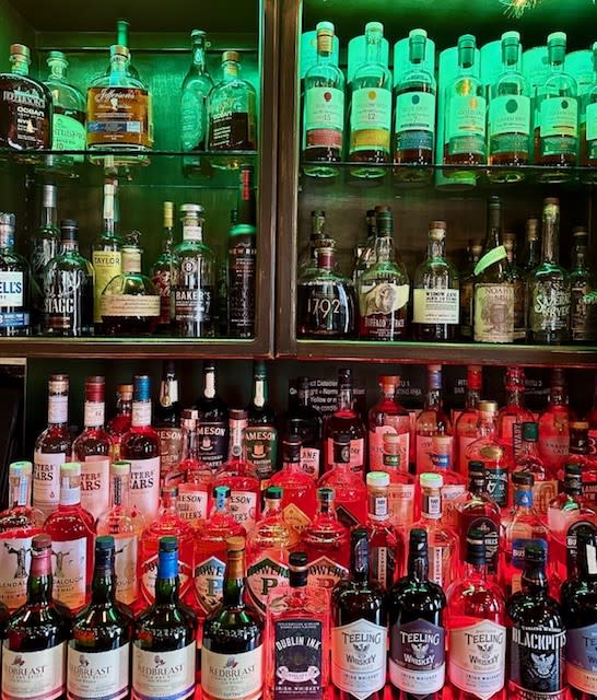 Dublin Village Tavern shelves stocked with a wide variety of whiskey bottles, illuminated by green and red lighting.