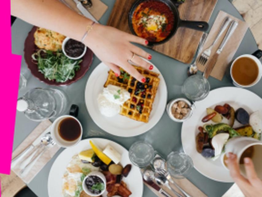 Overhead view of a shared brunch table with waffles, eggs, coffee, and breakfast dishes being served