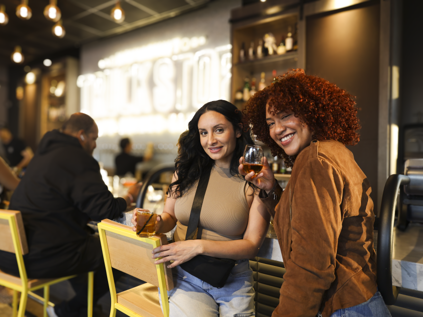 Two friends enjoying drinks and conversation at a stylish Fayetteville bar with warm lighting and a relaxed, modern vibe.