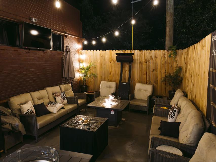 Cozy outdoor lounge with cushioned wicker seating, string lights overhead, and a glowing firepit table on a crisp fall night in Fayetteville, NC.