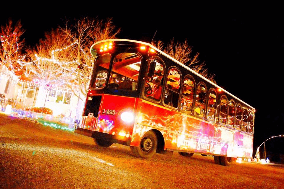 A photo of a Cheyenne Street Railway trolley driving down a snowy street at night. The trolley is decorated with Christmas lights, and the street is lined with snow-covered trees and buildings.