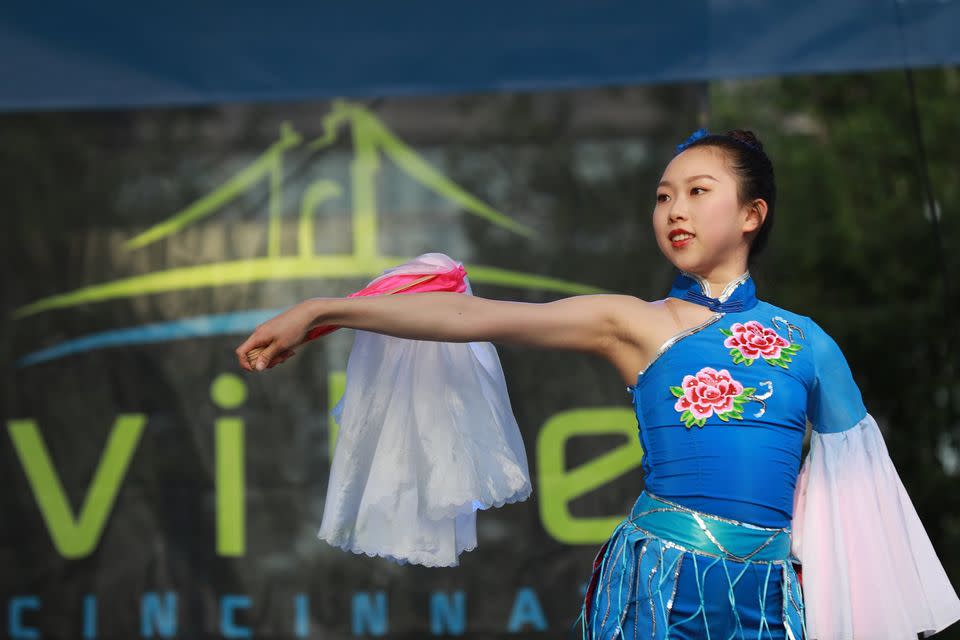 Young Asian woman in a blue dress with red flowers in front of a sign that reads Vibe Cincinnati