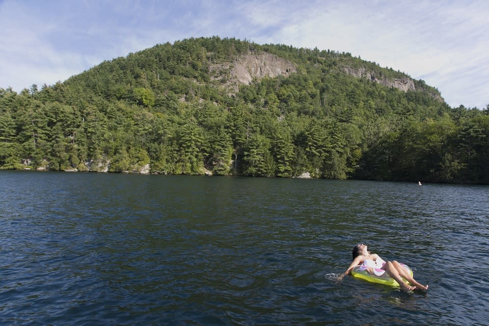 Woman floating on a tube in a Lake George Bay with a mountain in the background