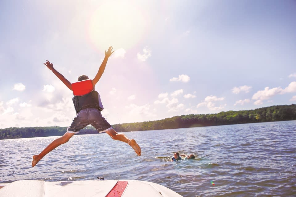 Person jumping off a boat into Lake George while others swim in the lake