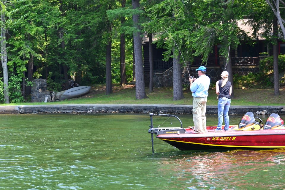 Couple fishing from a boat on Lake George with a summer camp in the background