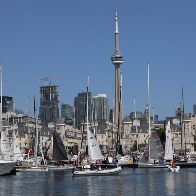 Toronto Harbour with CN Tower in background with several sailboats and people walking by marina