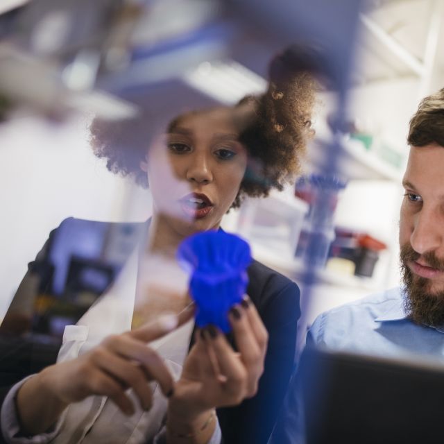 Man and woman inspect blue object printed with 3D printer