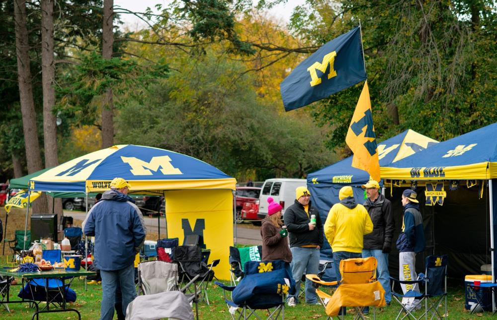 University of michigan flags and tents stand as people sit and stand around having conversations.