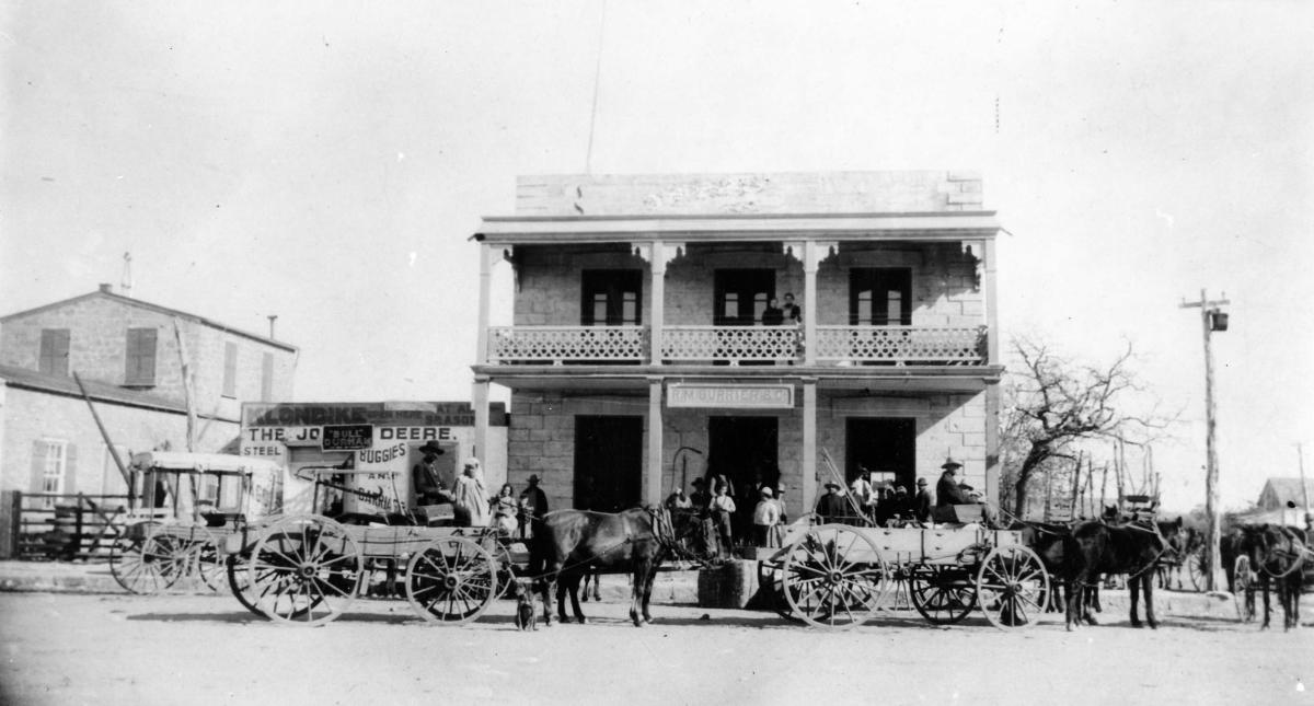 In an old B&W photo, horse-drawn carts are stopped in front of the The Priess Building/Keidel Memorial Hospital