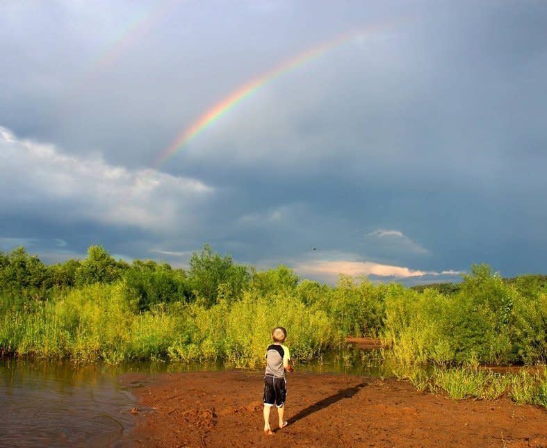 rainbow over a muddy beach area with a child looking at it.
