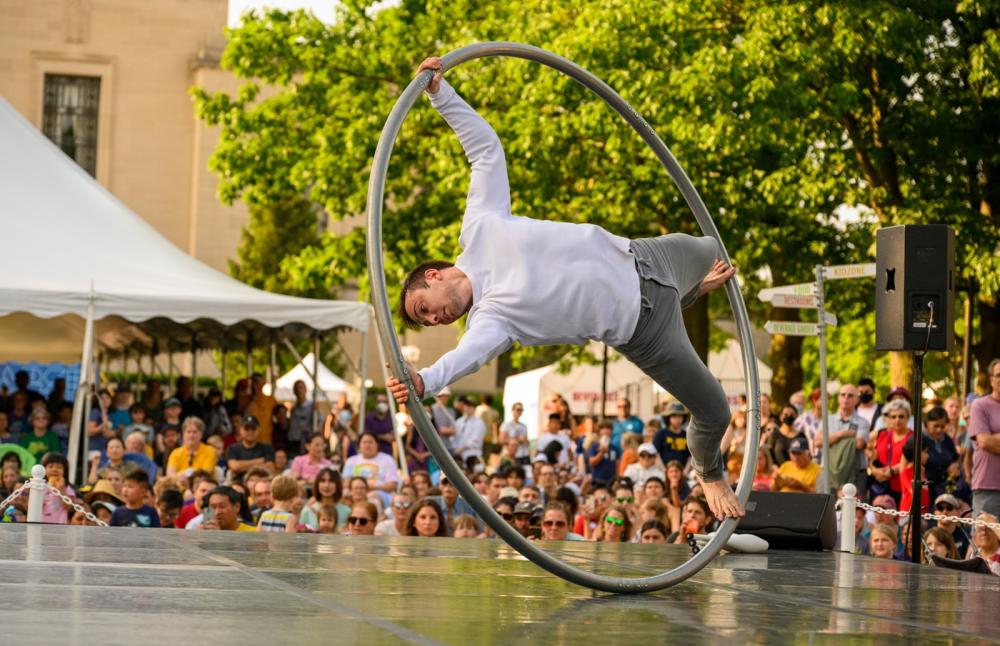 Person performs acrobats on stage with large hulla hoop ring. Audience watches in excitement.