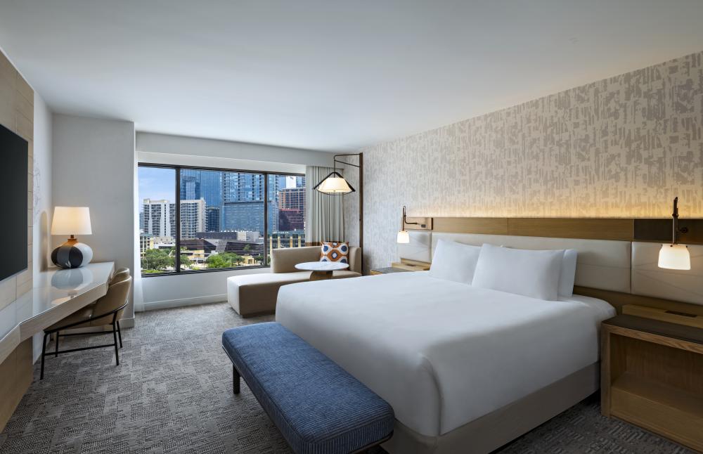 Image of a hotel room with a bed and couch with a window overlooking downtown Austin.