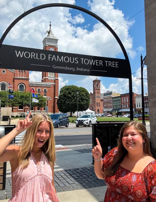 two girls pointing at the decatur county courthouse tree in the tower with archway in the background that says "world famous tower tree"
