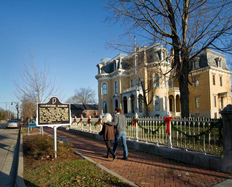 Visitors walk down the sidewalk outside of Culbertson Mansion during winter in New Albany, IN