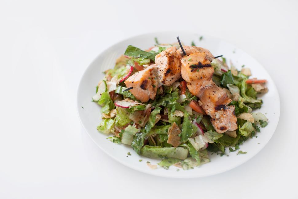 A large, white bowl of green salad with big pieces of salmon on top