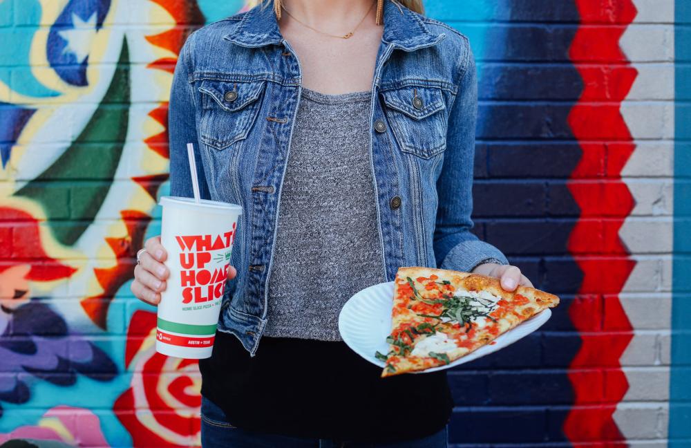 Woman holding a slice of pizza and a soda outside of Home Slice Pizza on South Congress