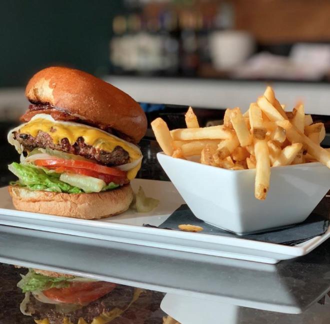 Plate with burger filled with cheese, meat, tomato and lettuce, served with a side of French fries