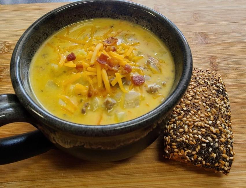 A mug of soup topped with bacon and a side of seeded bread