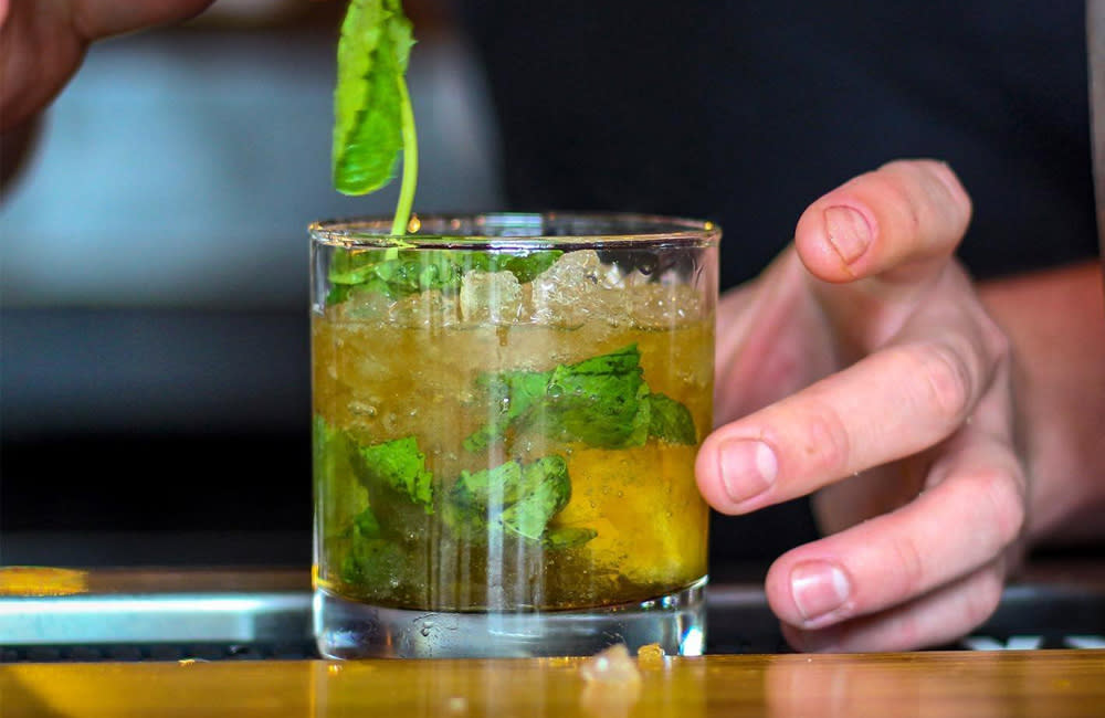 A man's hand adds a spring of mint to a cocktail glass with a mint julep on ice