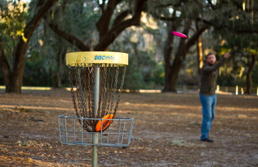 Man Throwing A Disc Golf Disk At The Basket On People Enjoying Virtual Golf At Top Golf On St. Simons Island, GA