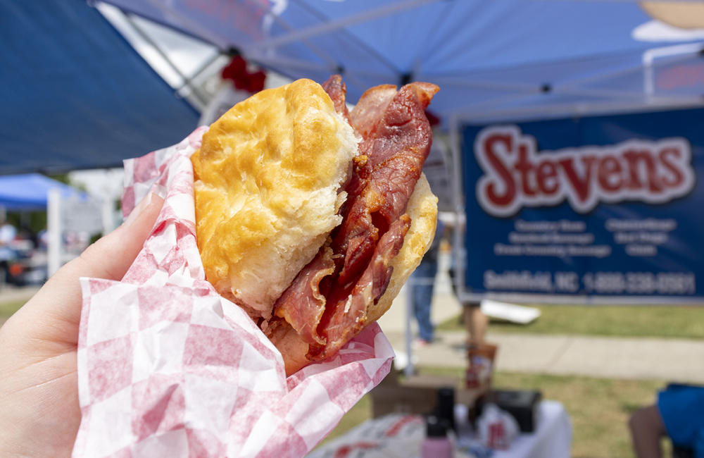 A ham biscuit is held up in front of the Stevens Sausage sign at the Smithfield Ham & Yam Festival.