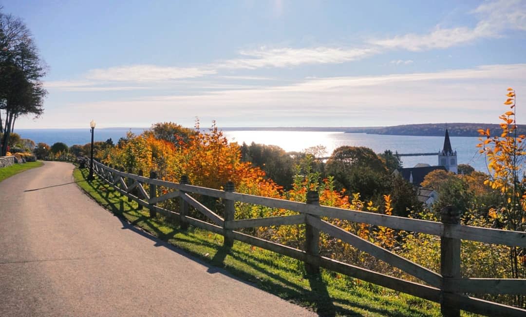 A Mackinac Island road and fence in the morning sun shining over Lake Huron in autumn
