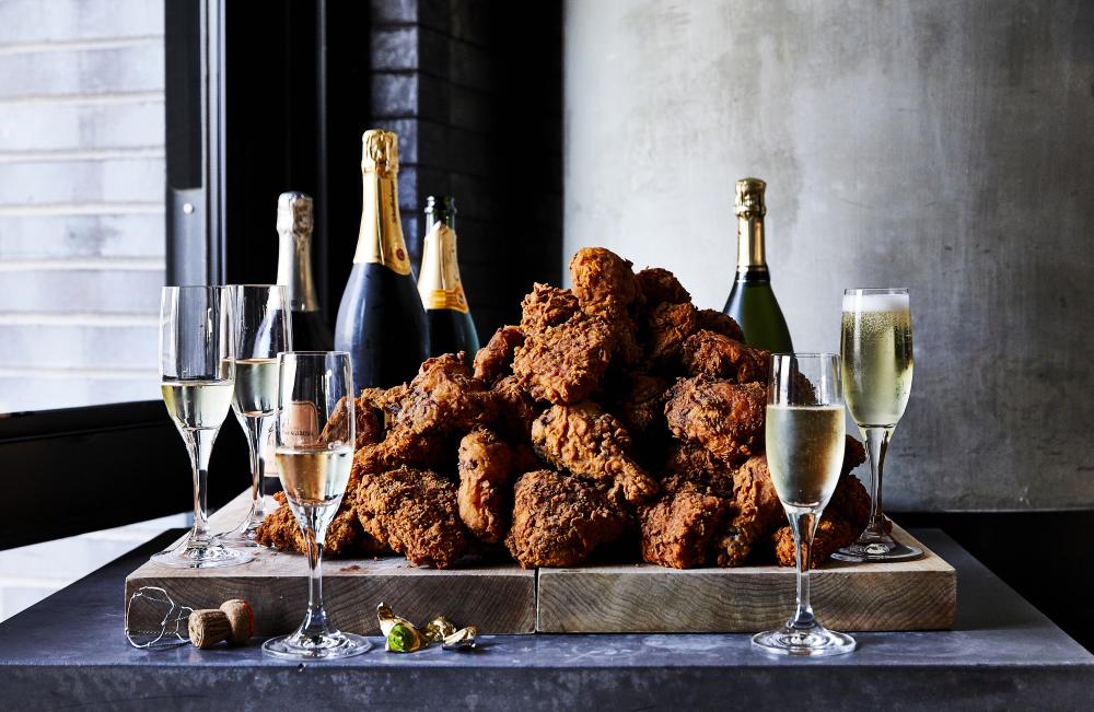 A giant platter of crispy fried chicken surrounded by glasses of champagne.