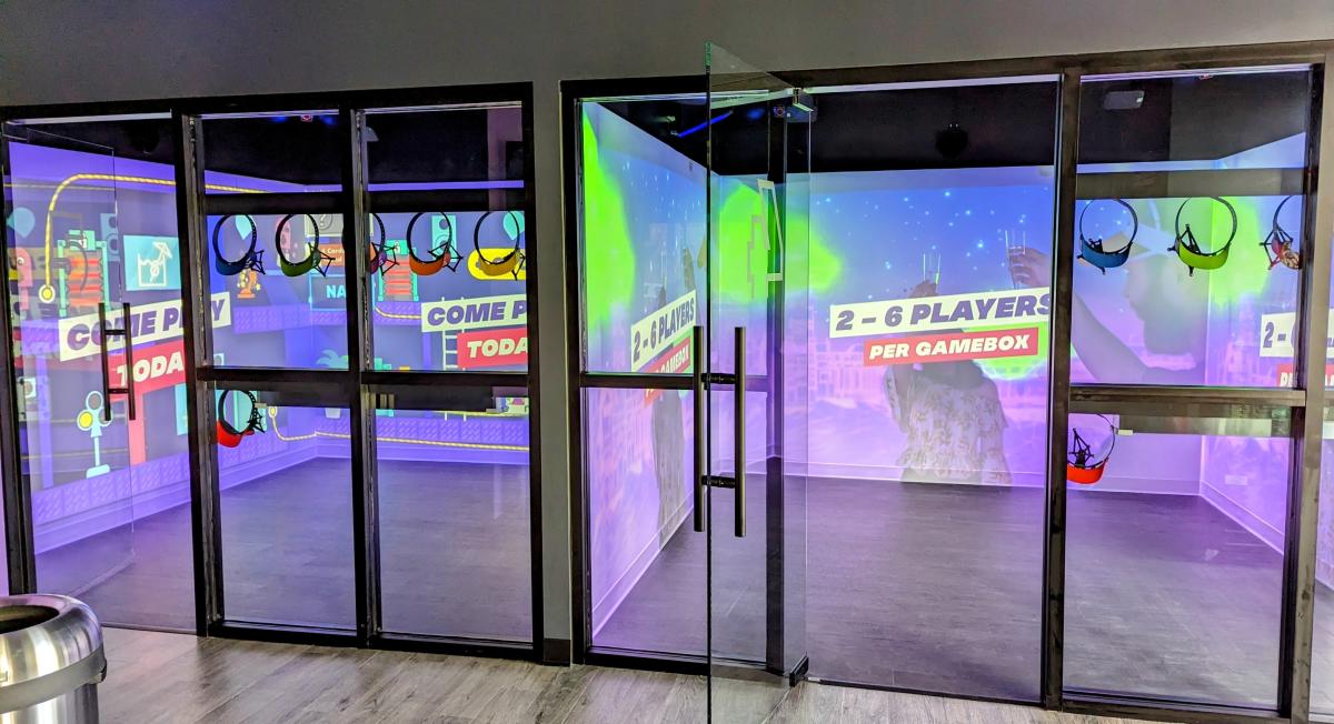 Image is of looking inside two glass rooms with games projected on the solid walls that surround the box on three sides.