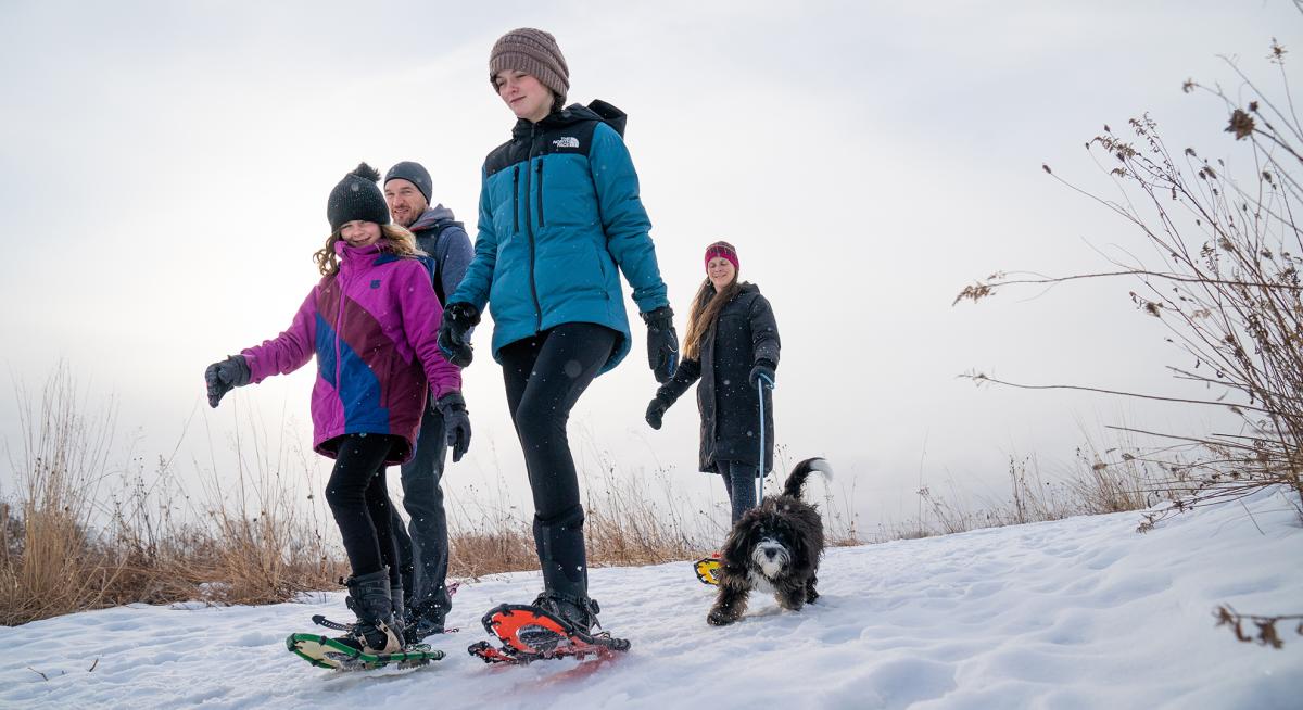 A family and their dog snowshoeing on a trail at Pheasant Branch Conservancy