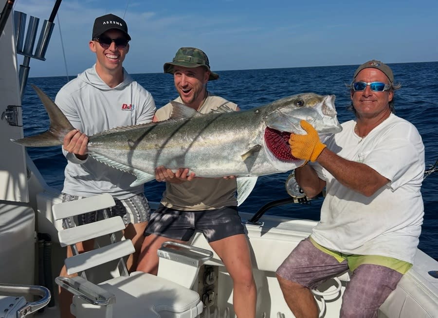 Three guy friends holding a large fish aboard a fishing charter.