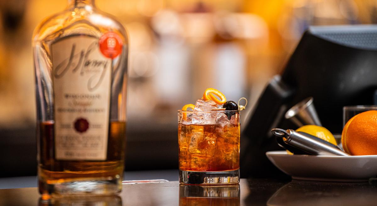 A bottle of J. Henry & Sons bourbon sits next to a hand-crafted cocktail