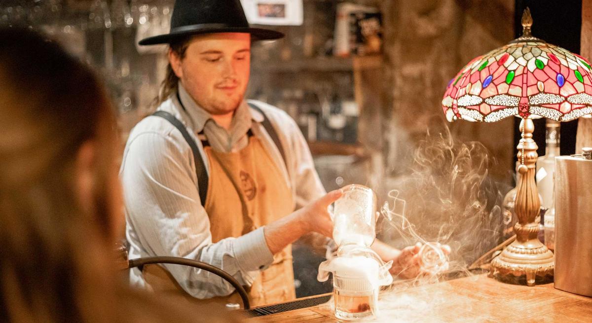 Bartender pouring a smoked beverage at the Blind Lion Speakeasy