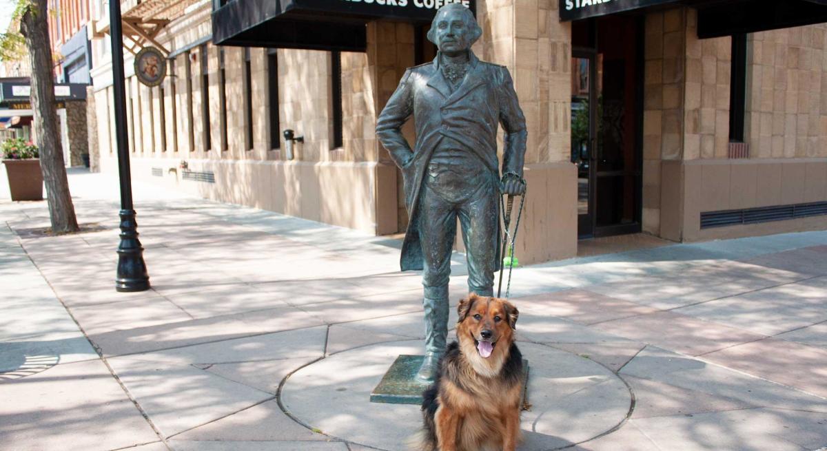 Dog sitting with George Washington's statue in Downtown Rapid City