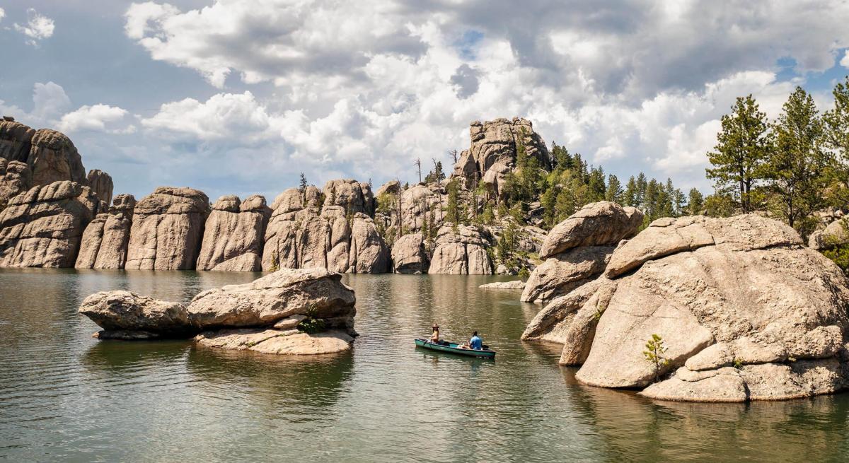 couple canoeing on the waters of sylvan lake in custer state park with the granite spires behind them