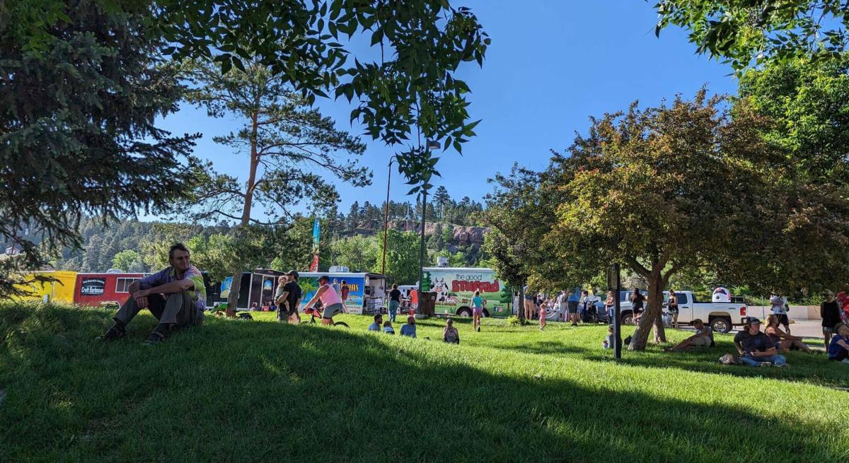 People scatter across the grass of canyon lake park with food trucks in the background