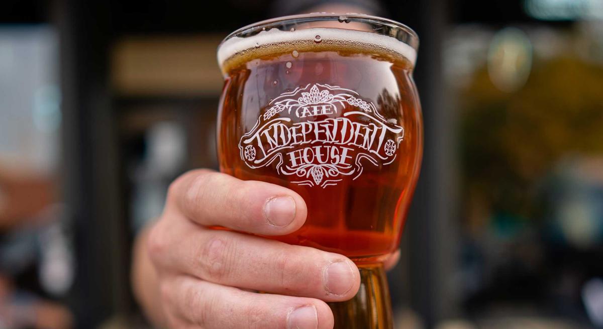 Hand holding Independent Ale House glass towards camera