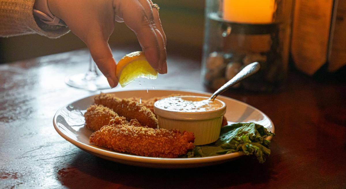 Plate of breaded walleye fingers with lemon juice being squeezed on them