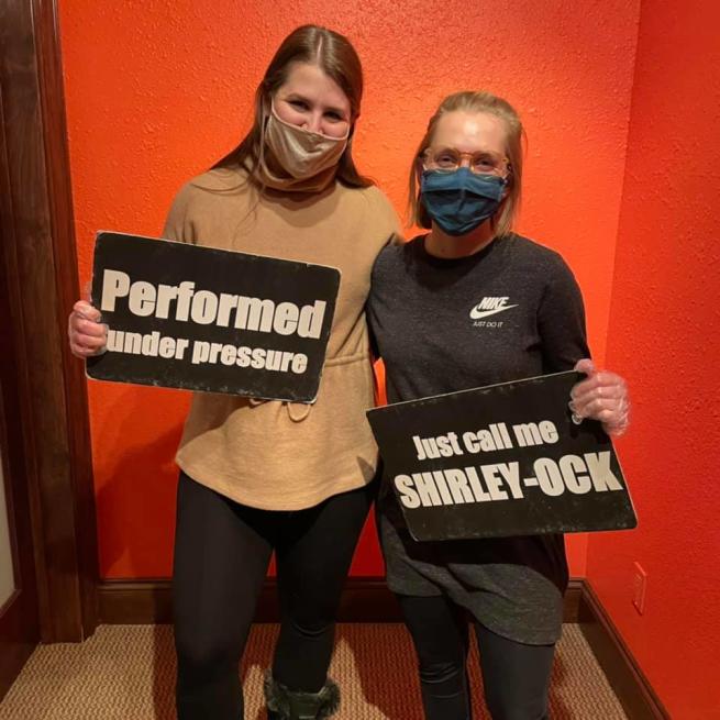 Two women holding signs after completing an escape room at Escape This