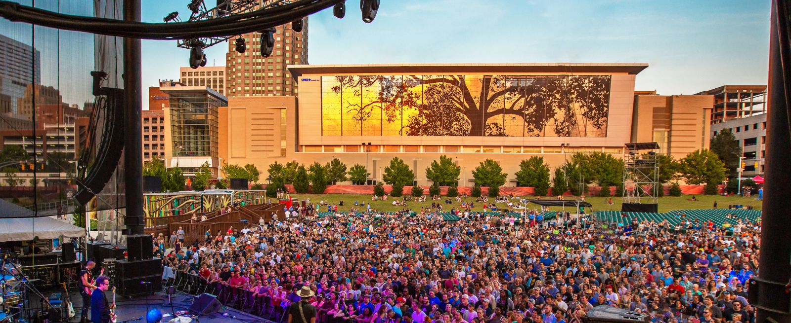 Large crowd at outside amphitheater concert with Raleigh skyline in background