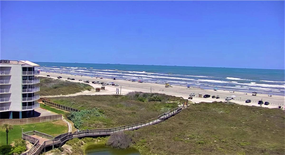 Photo of the view from a webcam showing the sand dunes, a boardwalk, and the beach.