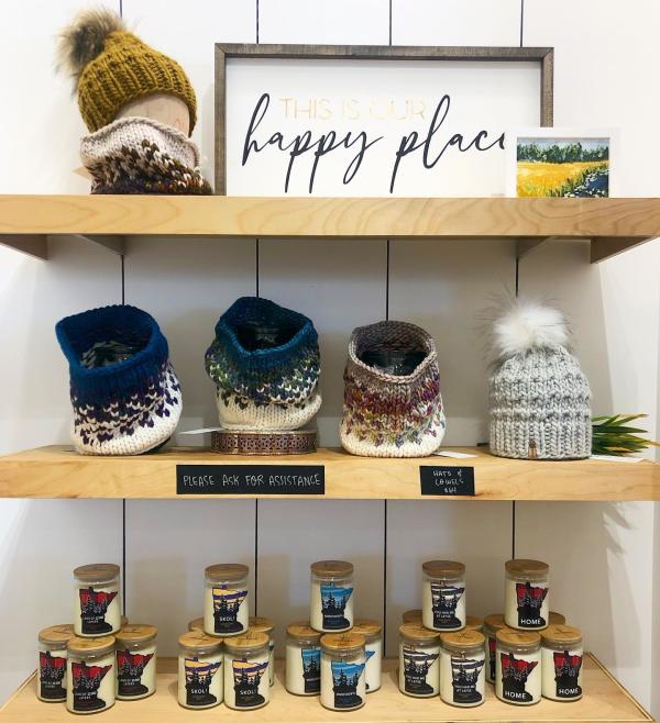 Shelves of knit caps and candles with a sign that says "This is Our Happy Place"